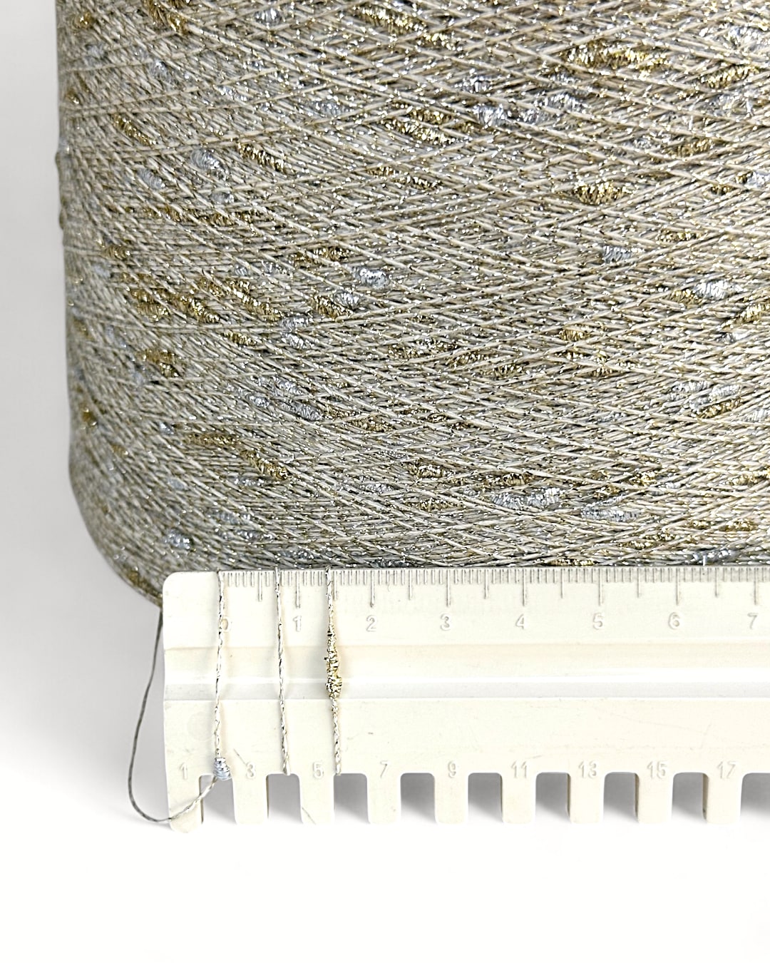 Close-up of a spool of glittery thread with a ruler for scale on a white background