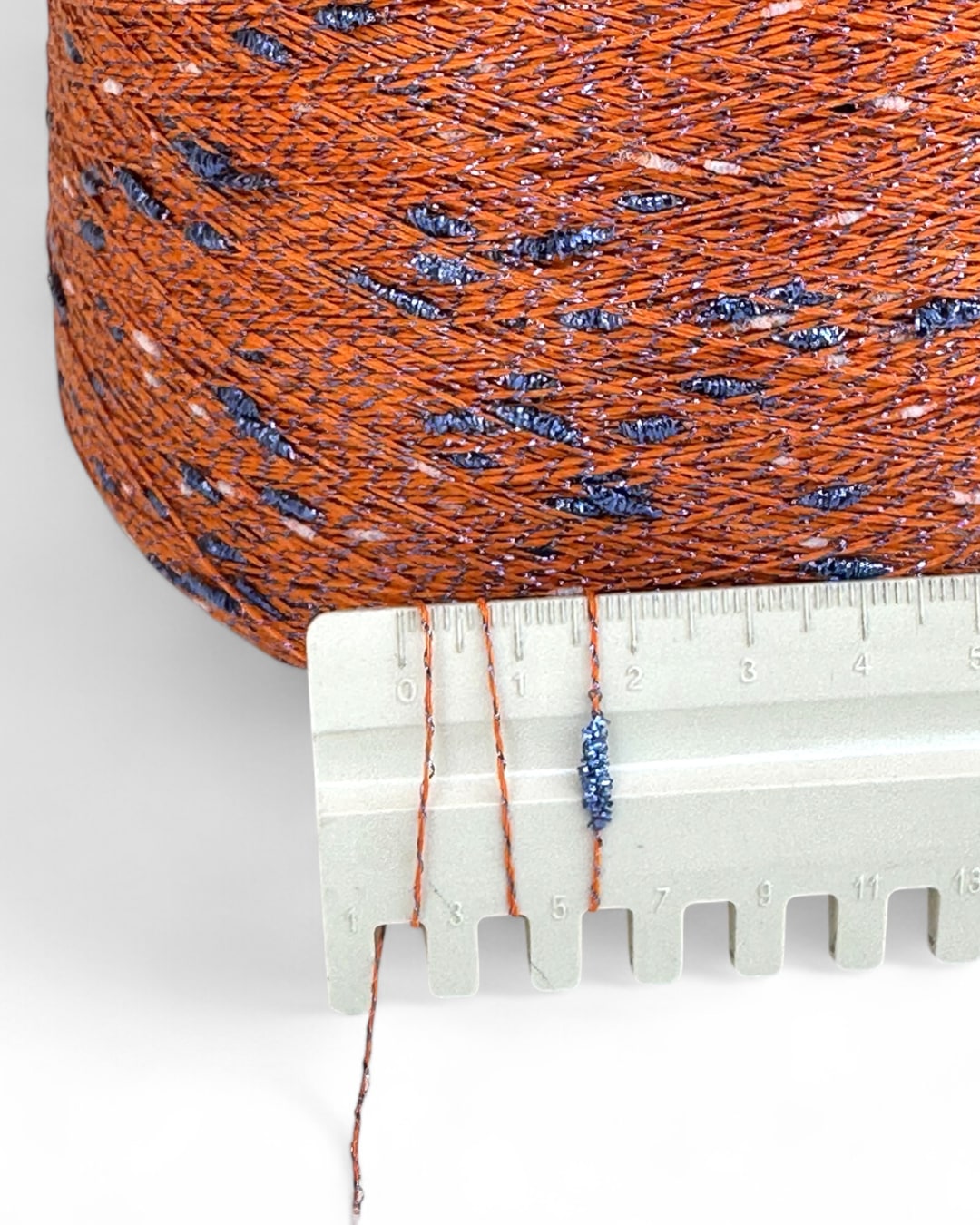 Spool of orange and blue thread with a ruler showing measurement