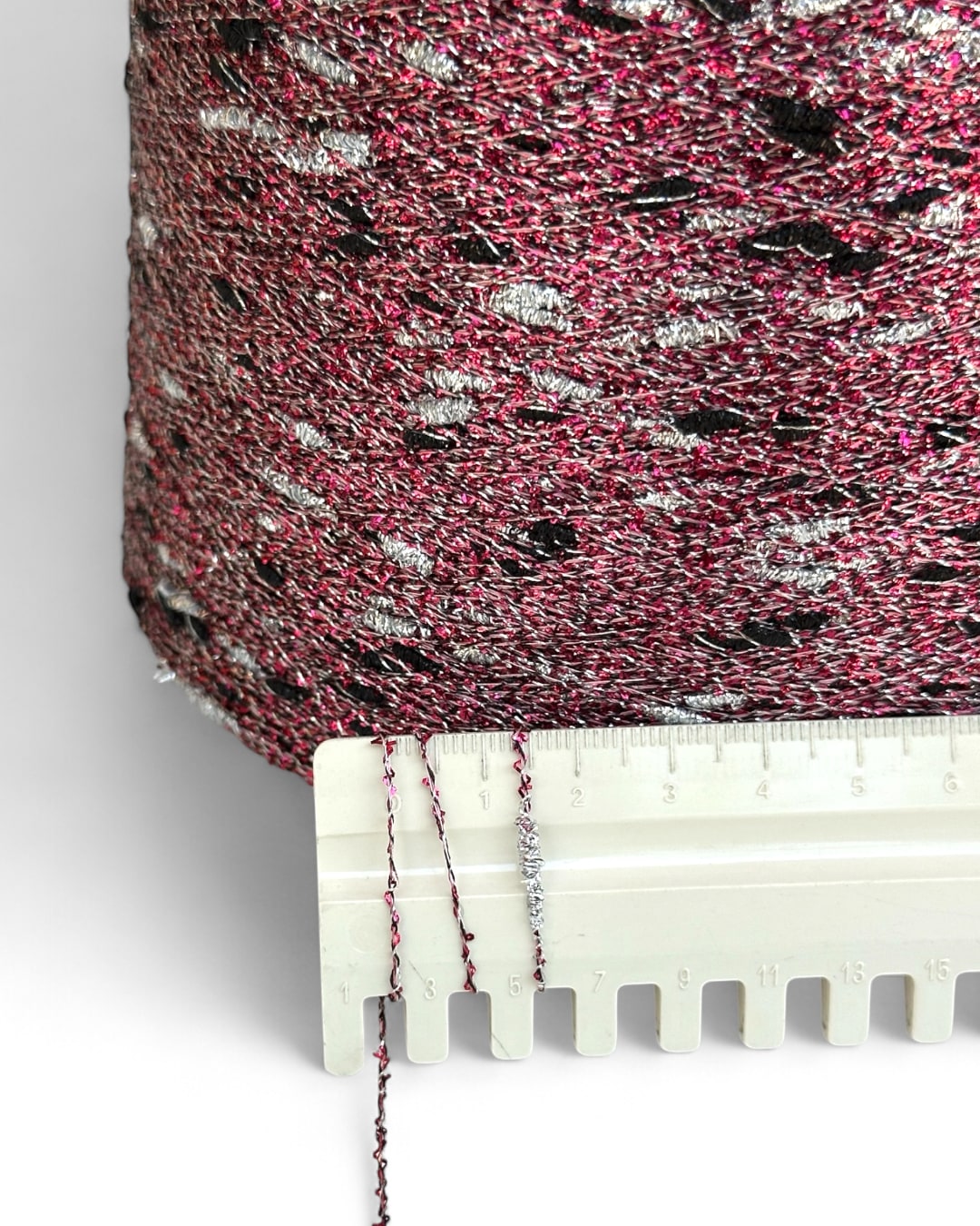 Close-up of pink yarn with black and white specks, held by a white plastic tool against a white background.