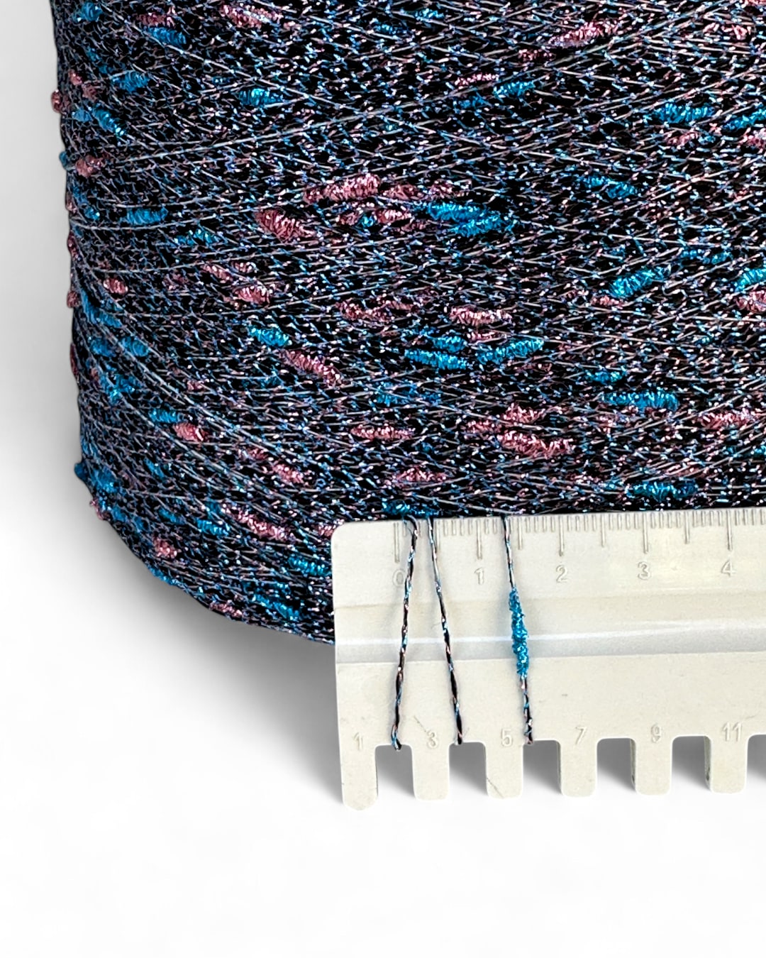 Close-up of a spool of black thread with blue and pink specks, next to a ruler for scale.