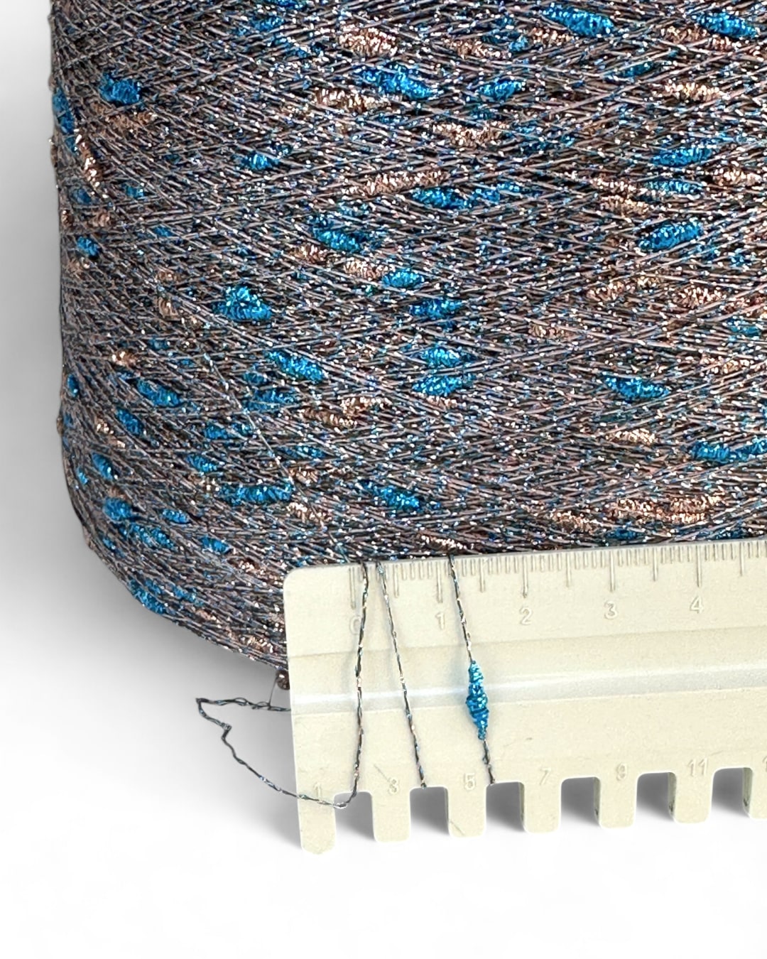 Close-up of a spool of blue and gray thread with a ruler for scale on a white background