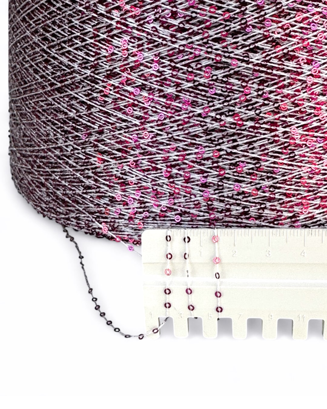 Spool of pink and gray yarn with a measuring tape for scale on a white background