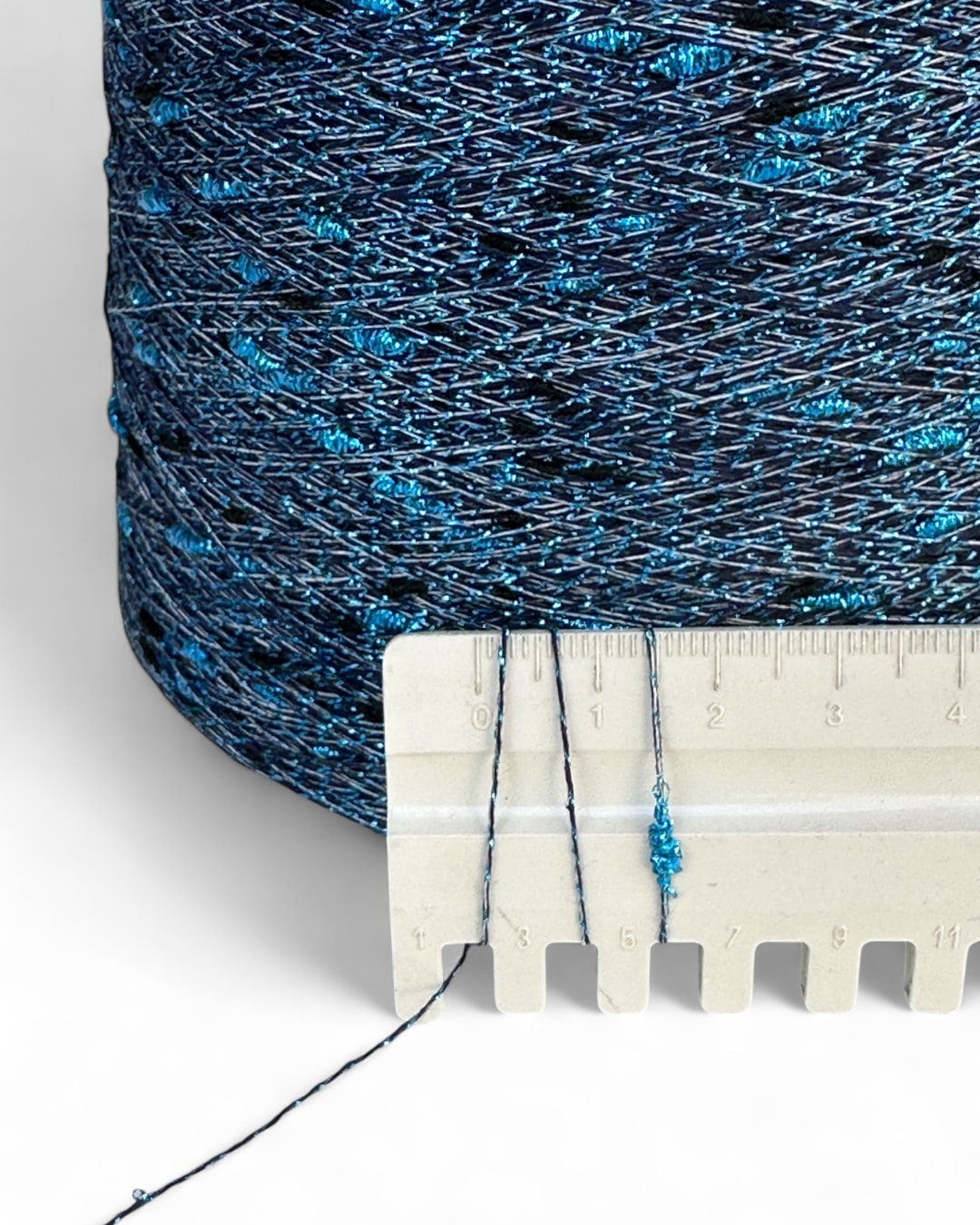 Spool of blue thread with a ruler for scale on a white background