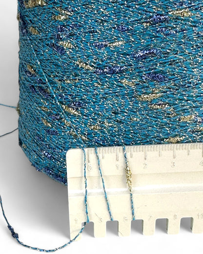 Close-up of blue yarn with gold accents on a white background, next to a ruler for scale.