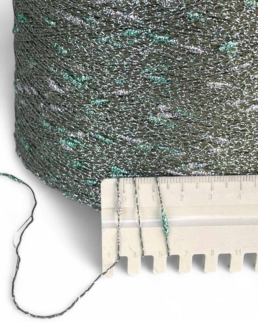 Close-up of a spool of green and silver metallic thread with a ruler for scale.