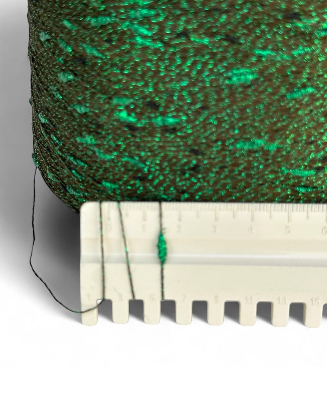 Close-up of green textured fabric with a white plastic strip underneath on a gray background