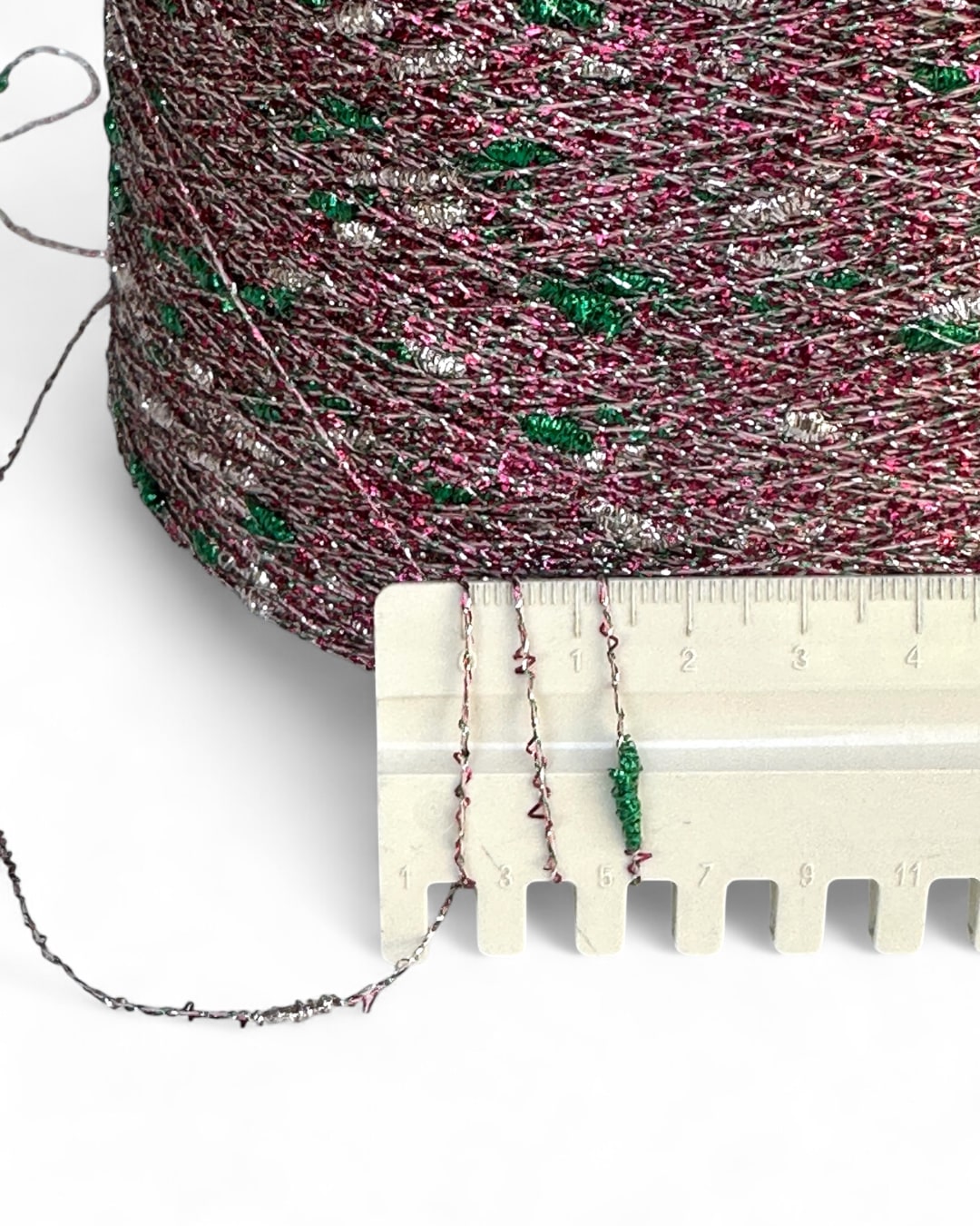 Spool of multicolored thread with a ruler for scale on a white background