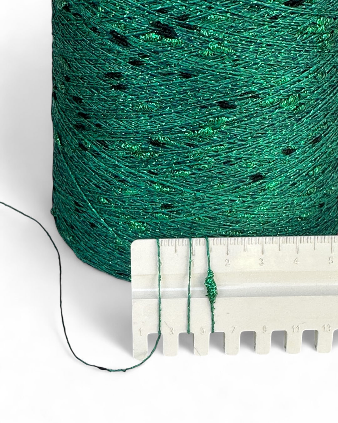 Green spool of thread with a ruler for scale on a white background