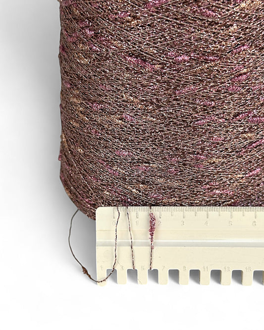 Close-up of a spool of brown thread with pink specks, next to a wooden ruler for scale.