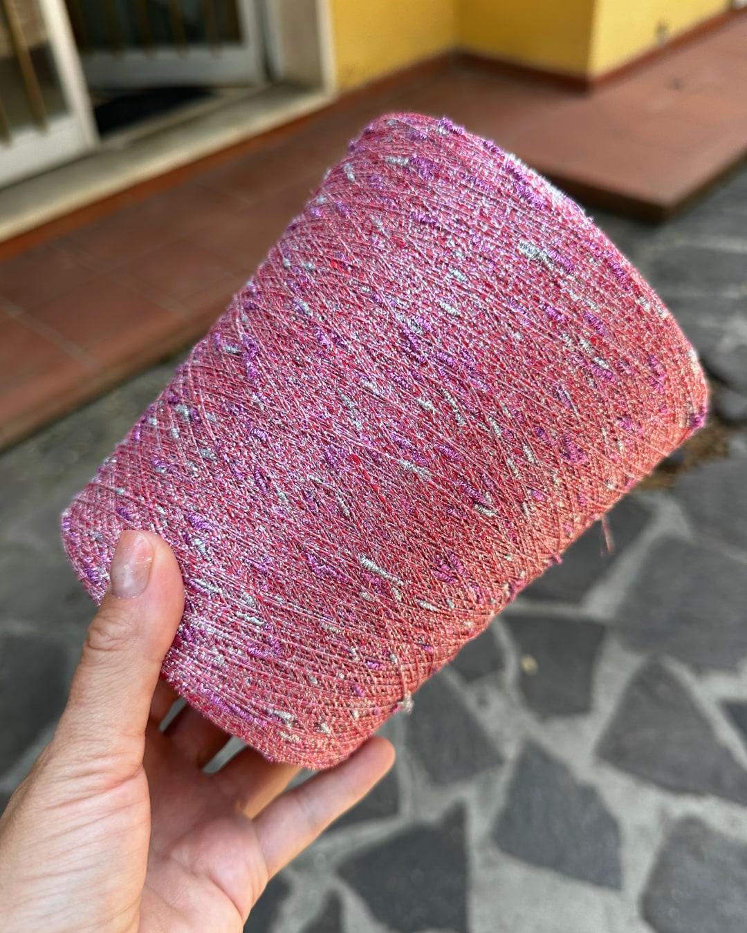 Pink glittery fabric roll held by a hand on a stone pavement.