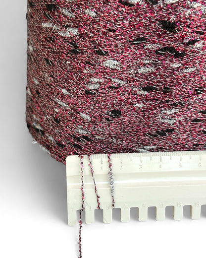 Close-up of pink yarn with black and white specks, held by a white plastic tool against a white background.