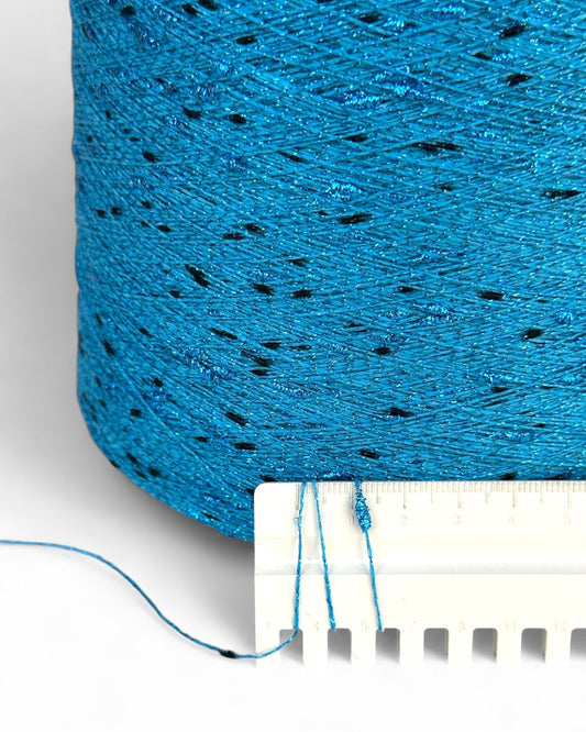 Close-up of blue yarn with black specks and a measuring tape for scale.