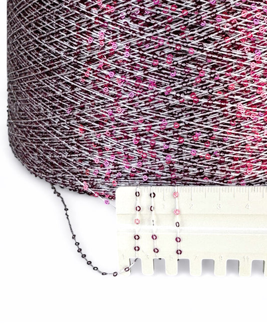 Spool of pink and gray yarn with a measuring tape for scale on a white background