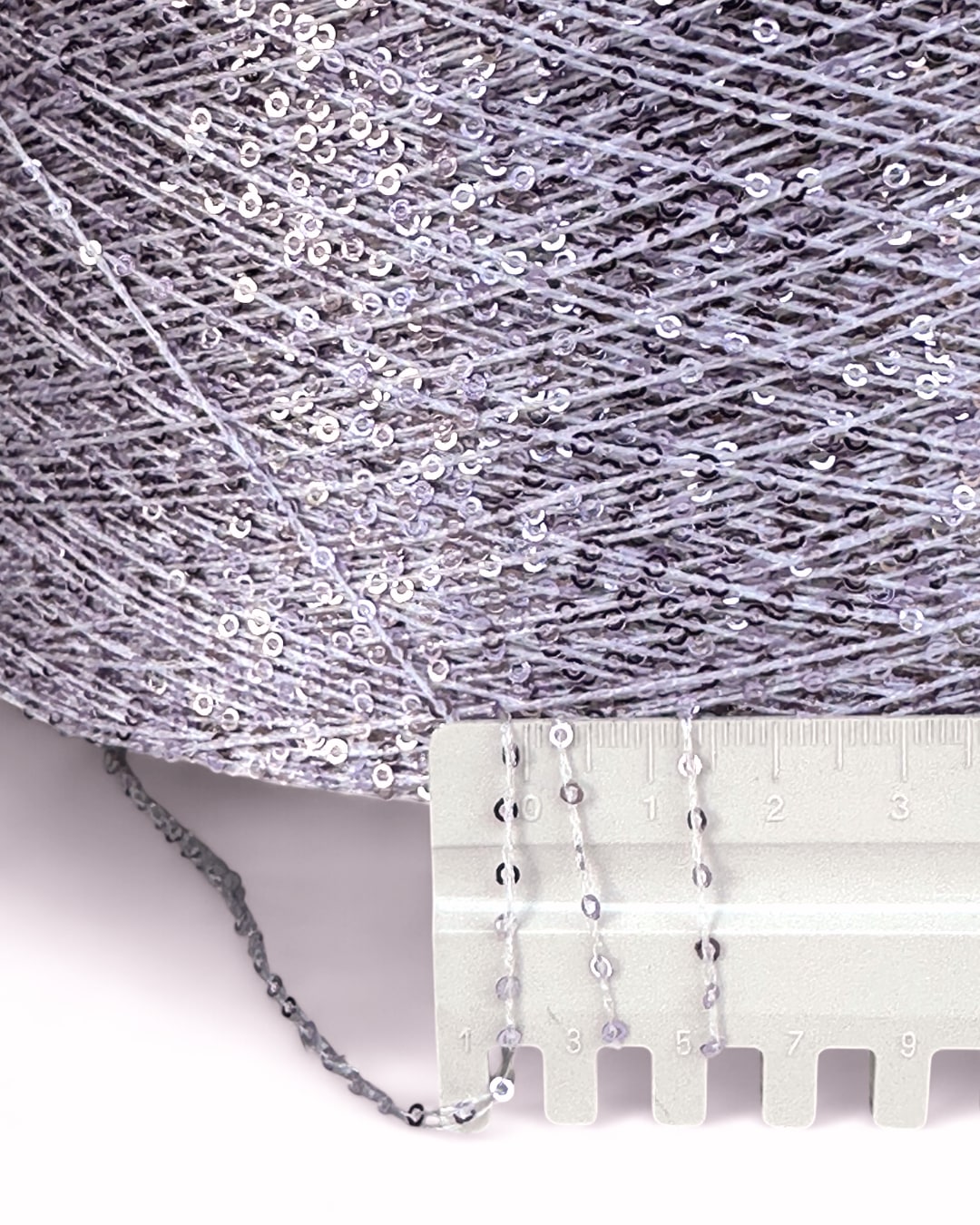 Close-up of silver sequin fabric with a measuring tool on a white background