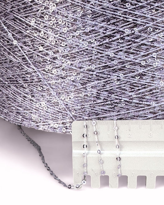 Close-up of silver sequin fabric with a measuring tool on a white background