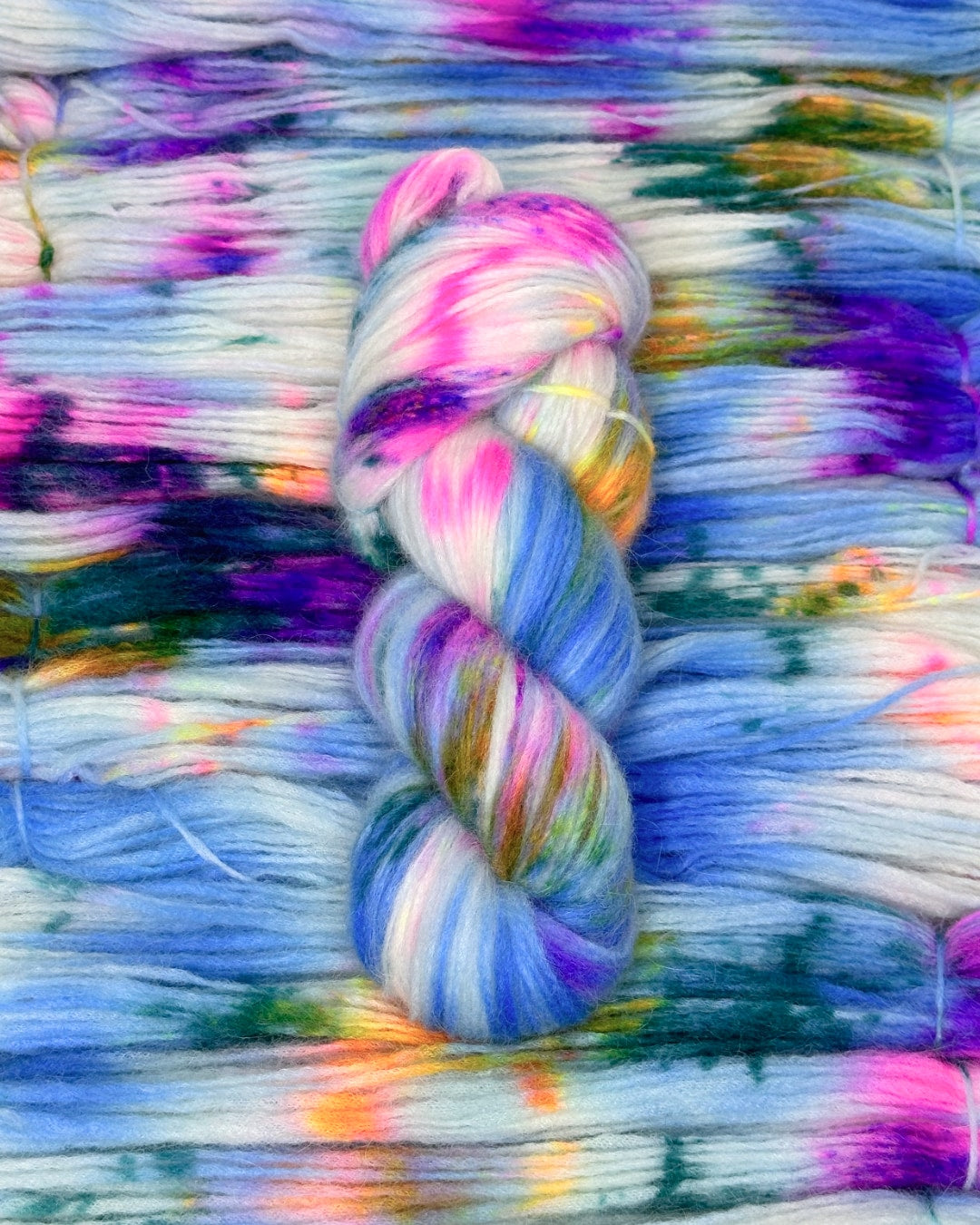 A vibrant skein of luxury hand-dyed yarn featuring a mix of blue, purple, pink, yellow, and white hues. Made from super baby alpaca fiber blended with merino wool and nylon for durability and softness. Each skein measures 400 meters in length per 100 grams weight.