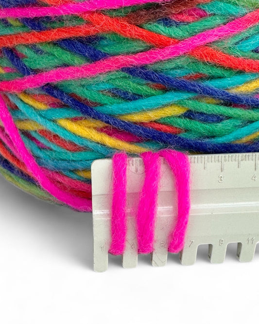 Multicolored yarn ball with a clear plastic knitting needle and ruler on a white background